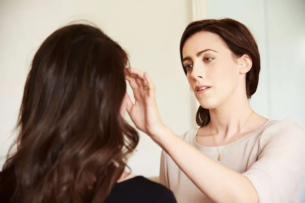 One woman gently tapping beside another woman’s eyebrow