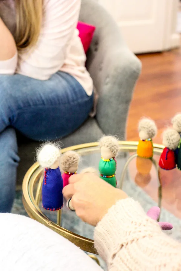Small peg figures with felt hats set out on a glass table, a hand moving one of them